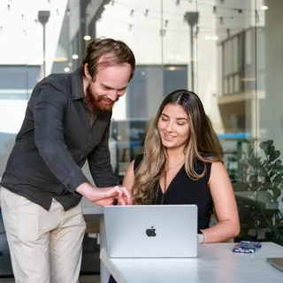 Two colleagues smiling as they review work on a laptop